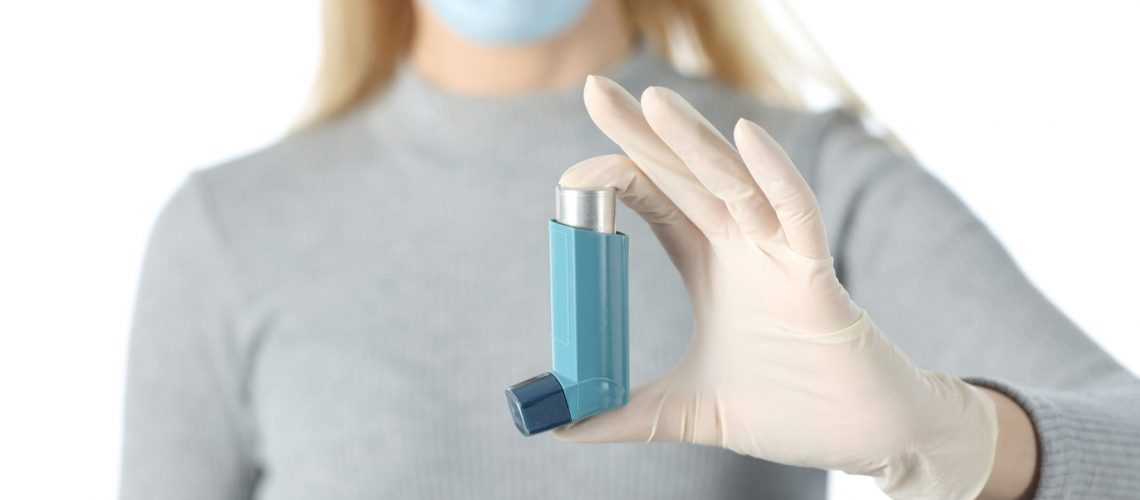 Close up front view of woman hand showing inhaler avoiding covid-19 with mask and glove isolated on white background